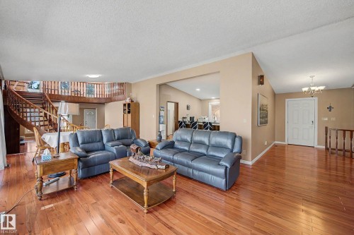 Expansive living area showcasing wood-finish flooring, a grand curved wooden staircase with a balustrade, a front entry door with side lites, and an overhead chandelier light fixture - 250 197 Avenue, Edmonton, AB - Indoor Photo Showing Living Room