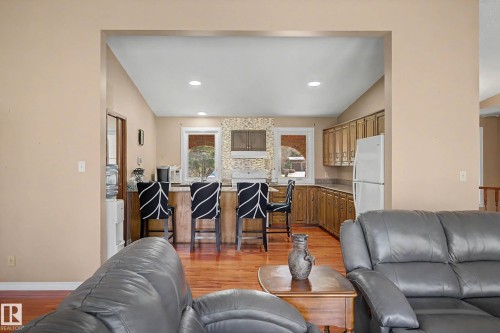 Kitchen featuring wood-finish flooring, a breakfast bar, recessed lighting, wood cabinetry, and a tile backsplash - 250 197 Avenue, Edmonton, AB - Indoor Photo Showing Living Room