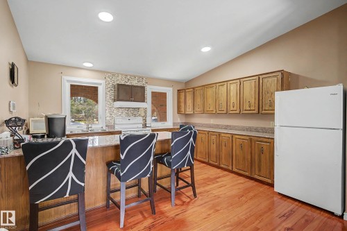 Kitchen featuring a breakfast bar with stone-look countertop, wood-finish cabinetry, a white electric range, and a white refrigerator - 250 197 Avenue, Edmonton, AB - Indoor Photo Showing Kitchen
