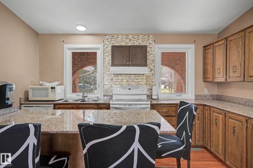 Kitchen featuring a central island with a granite-style countertop, wood cabinetry, a tile backsplash, and dual windows - 250 197 Avenue, Edmonton, AB - Indoor