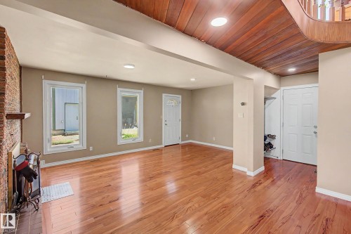 Expansive room featuring glossy wood-finish flooring, a brick-faced fireplace with a wooden mantel, multiple windows, recessed lighting, and a wood-paneled ceiling detail - 250 197 Avenue, Edmonton, AB - Indoor Photo Showing Other Room