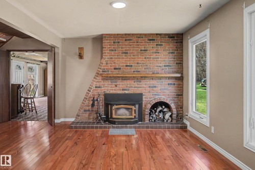 Brick-surround fireplace with wood stove insert and integrated wood storage niche, featuring a wood mantel - 250 197 Avenue, Edmonton, AB - Indoor Photo Showing Living Room With Fireplace