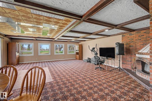 Spacious room with patterned carpet flooring, exposed wood beam ceiling, multiple windows, and a brick fireplace with hearth - 250 197 Avenue, Edmonton, AB - Indoor