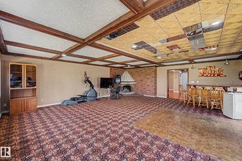 Spacious room featuring exposed ceiling beams, a brick-surround fireplace, and a built-in bar area - 250 197 Avenue, Edmonton, AB - Indoor