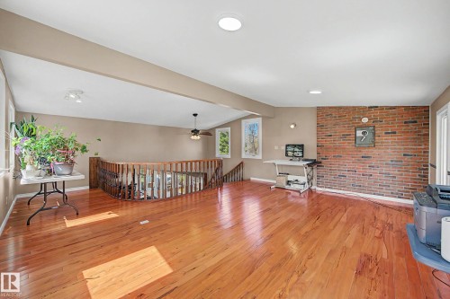 Spacious open-concept room featuring wood-finish flooring, a brick accent wall, and multiple windows - 250 197 Avenue, Edmonton, AB - Indoor Photo Showing Other Room