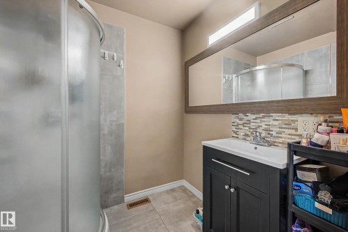 Bathroom featuring a curved glass shower enclosure with gray tile surround, dark wood-framed mirror, vanity with white countertop and black cabinetry, and mosaic tile backsplash - 250 197 Avenue, Edmonton, AB - Indoor Photo Showing Bathroom