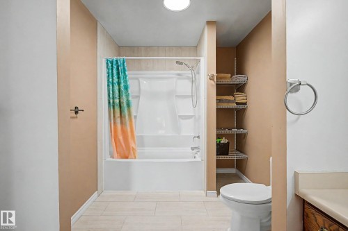 Full bathroom featuring a tub and shower combination with light-toned wall tile, a commode, and built-in shelving - 250 197 Avenue, Edmonton, AB - Indoor Photo Showing Bathroom