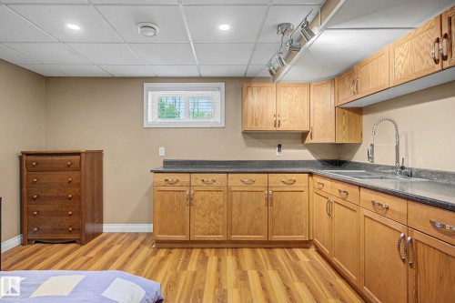 Lower level kitchenette featuring wood-finish flooring, light wood cabinetry, dark countertops, a double basin sink with a high arc faucet, and recessed lighting - 250 197 Avenue, Edmonton, AB - Indoor