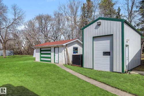 Two detached outbuildings featuring a white stucco structure with a red shingle roof and a green-striped garage door, alongside a larger metal-sided building with a green-trimmed roof and an overhead door - 250 197 Avenue, Edmonton, AB - Outdoor