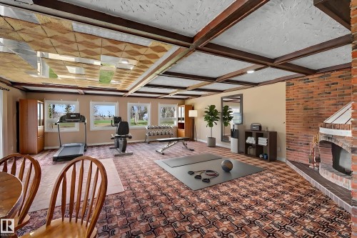 Spacious room featuring a brick fireplace, patterned carpet flooring, and exposed ceiling beams - 250 197 Avenue, Edmonton, AB - Indoor With Fireplace