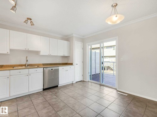 Kitchen featuring white cabinetry, a stainless steel dishwasher, light-toned countertops, and tile flooring - 17 15128 22 Street, Edmonton, AB - Indoor Photo Showing Kitchen With Double Sink