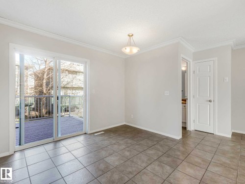 Spacious room featuring neutral-toned tile flooring, crown molding, and a sliding glass door opening to an outdoor deck - 17 15128 22 Street, Edmonton, AB - Indoor Photo Showing Other Room