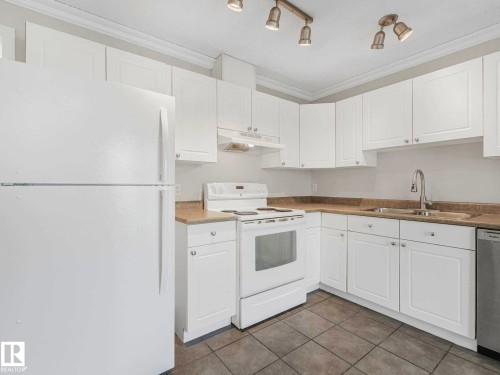 Kitchen featuring white cabinetry, light-toned countertops, a stainless steel sink with a gooseneck faucet, a white range, and a white refrigerator - 17 15128 22 Street, Edmonton, AB - Indoor Photo Showing Kitchen With Double Sink
