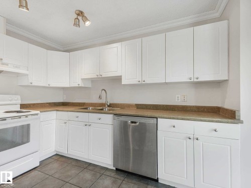 Kitchen featuring white cabinetry, a stainless steel dishwasher, a white range, a dual-basin sink with a chrome faucet, and tile flooring - 17 15128 22 Street, Edmonton, AB - Indoor Photo Showing Kitchen With Double Sink