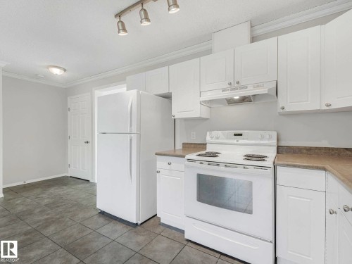 Kitchen featuring white cabinetry, range with overhead hood, refrigerator, light-toned countertops, and track lighting - 17 15128 22 Street, Edmonton, AB - Indoor Photo Showing Kitchen