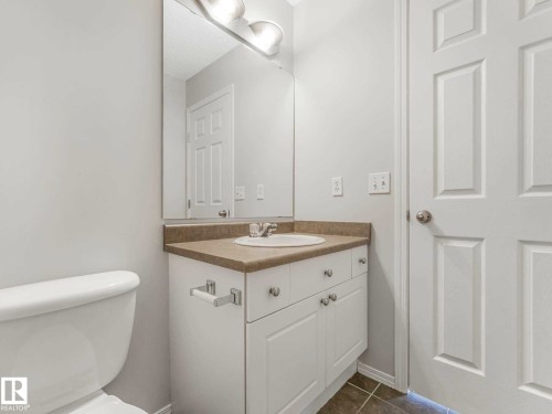 Bathroom featuring a white vanity with a tan countertop, an integrated sink, a wall-mounted mirror, and white paneled doors - 17 15128 22 Street, Edmonton, AB - Indoor Photo Showing Bathroom