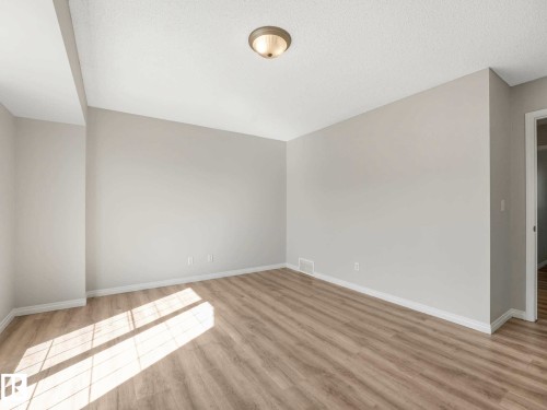 Spacious room featuring light wood-finish flooring, neutral wall tones, white baseboards, and a flush-mount ceiling light - 17 15128 22 Street, Edmonton, AB - Indoor Photo Showing Other Room