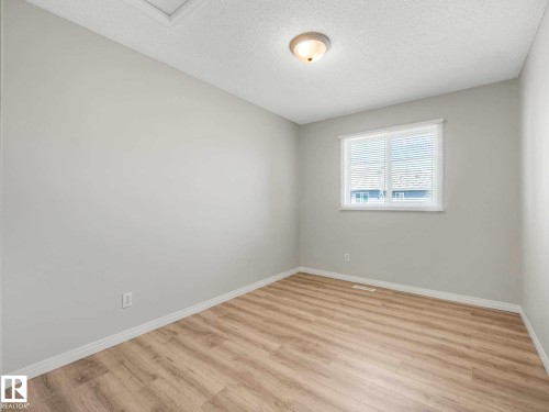 Neutral-toned room featuring light wood-finish flooring, white baseboards, and a single window with horizontal blinds - 17 15128 22 Street, Edmonton, AB - Indoor Photo Showing Other Room
