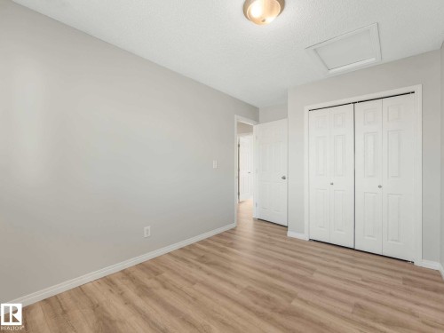 Room featuring wood-finish flooring, light gray wall paint, white baseboards, a flush-mount ceiling light, and white bi-fold closet doors - 17 15128 22 Street, Edmonton, AB - Indoor Photo Showing Other Room