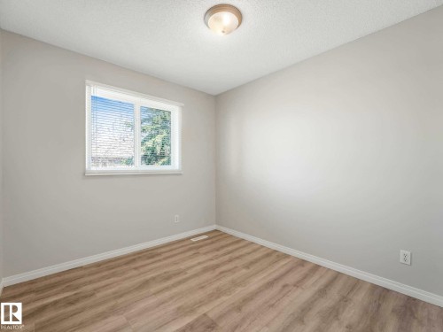 Room featuring a large window with white blinds, light wood-finish flooring, white baseboards, and neutral wall paint - 17 15128 22 Street, Edmonton, AB - Indoor Photo Showing Other Room