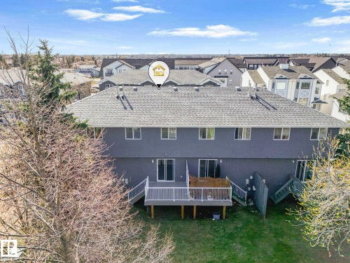 Rear exterior featuring a spacious wooden deck with white railings, multiple sliding glass doors, and a sloped lawn - 17 15128 22 Street, Edmonton, AB - Outdoor