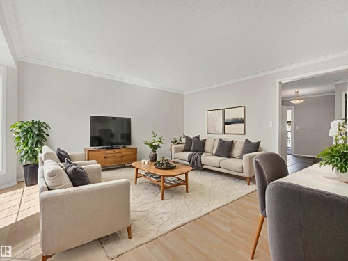 Spacious living area featuring light wood-finish flooring, white crown molding, and neutral wall tones - 17 15128 22 Street, Edmonton, AB - Indoor Photo Showing Living Room