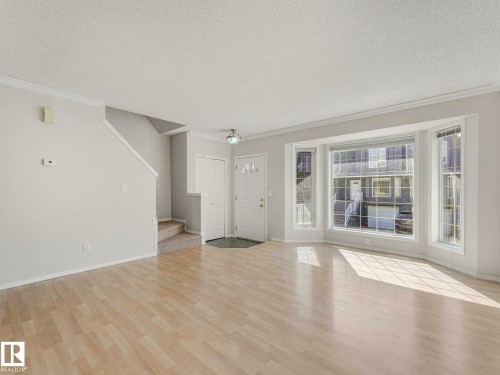 Entryway and living area featuring wood-finish flooring, a prominent bay window, white baseboards, and crown molding - 17 15128 22 Street, Edmonton, AB - Indoor Photo Showing Other Room
