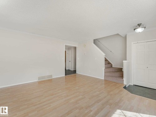 Spacious room featuring wood-finish flooring, white walls, and a staircase with carpeted treads - 17 15128 22 Street, Edmonton, AB - Indoor Photo Showing Other Room