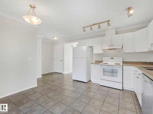 Kitchen featuring white cabinetry, light-toned countertops, and a white appliance suite - 17 15128 22 Street, Edmonton, AB - Indoor Photo Showing Kitchen With Double Sink