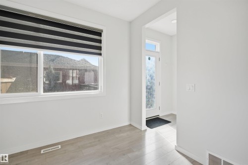 This room features light-colored flooring, a window with a striped privacy blind, and a white entrance door with a decorative glass panel - 2125 Maple Road Nw, Edmonton, AB - Indoor Photo Showing Other Room