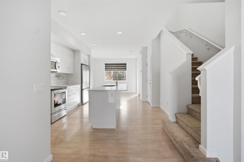 Open concept kitchen featuring an island with a sink, white cabinetry, and stainless steel appliances - 2125 Maple Road Nw, Edmonton, AB - Indoor Photo Showing Kitchen