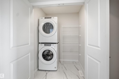 Dedicated laundry space featuring a stacked washer and dryer, wire shelving, and sleek tile flooring - 2125 Maple Road Nw, Edmonton, AB - Indoor Photo Showing Laundry Room