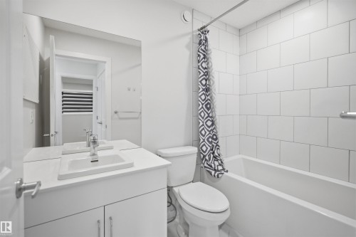 Well-appointed bathroom featuring a vanity with an integrated sink, a large mirror, a toilet, and a bathtub with white subway tile surround - 2125 Maple Road Nw, Edmonton, AB - Indoor Photo Showing Bathroom