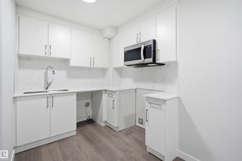 The kitchen features white cabinetry, a double basin stainless steel sink with a gooseneck faucet, a built-in microwave, and wood-style flooring - 2125 Maple Road Nw, Edmonton, AB - Indoor Photo Showing Kitchen