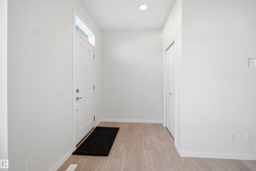 This entryway features light-colored flooring, a white paneled door with a transom window, and a closet with bifold doors - 2125 Maple Road Nw, Edmonton, AB - Indoor Photo Showing Other Room