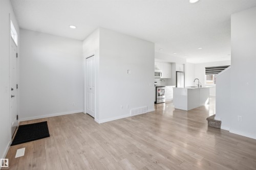 The property features light-toned flooring throughout, a modern kitchen with a white island and stainless steel appliances, and an entry door with an overhead window - 2125 Maple Road Nw, Edmonton, AB - Indoor Photo Showing Other Room