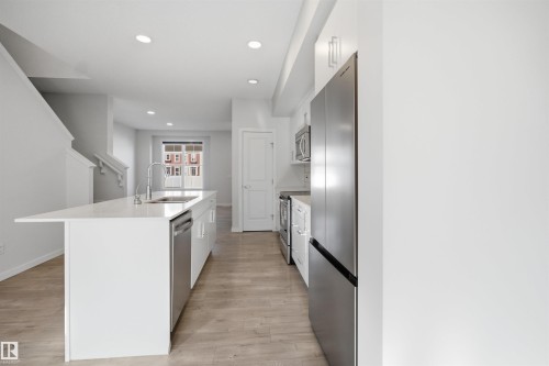Modern kitchen featuring light wood flooring, white cabinetry, stainless steel appliances, and a central island with a sink and a dishwasher - 2125 Maple Road Nw, Edmonton, AB - Indoor Photo Showing Kitchen