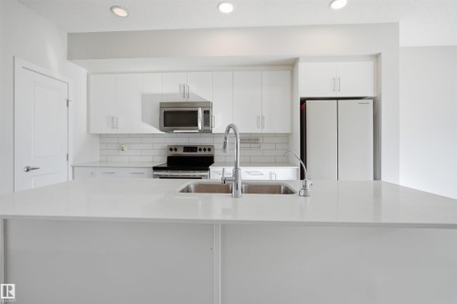 Modern kitchen with white cabinetry, stainless steel microwave, and white subway tile backsplash - 2125 Maple Road Nw, Edmonton, AB - Indoor Photo Showing Kitchen With Double Sink With Upgraded Kitchen