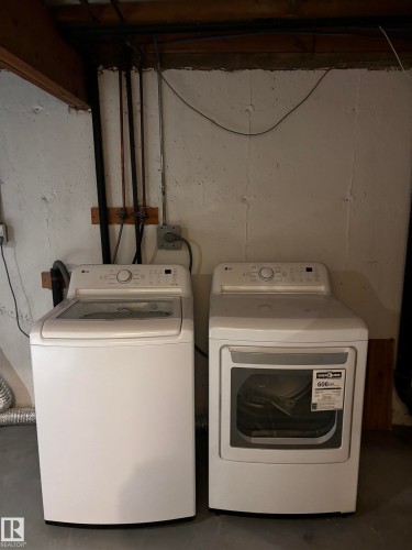 White top-load washer, white front-load dryer, concrete walls, concrete flooring, exposed overhead beams - 14075 30 Street Nw, Edmonton, AB - Indoor Photo Showing Laundry Room