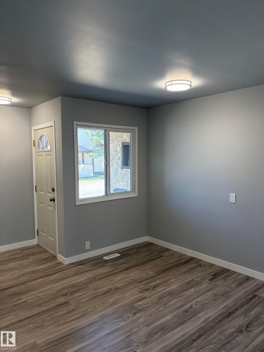 Spacious room featuring wood-finish flooring, light grey painted walls, white trim, and two contemporary flush-mount ceiling lights - 14075 30 Street E, Edmonton, AB - Indoor Photo Showing Other Room