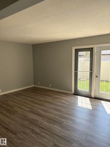 Spacious room with wood-finish flooring, light grey walls, and white baseboards - 14075 30 Street E, Edmonton, AB - Indoor Photo Showing Other Room