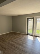 Spacious room with wood-finish flooring, light grey walls, and white baseboards - 