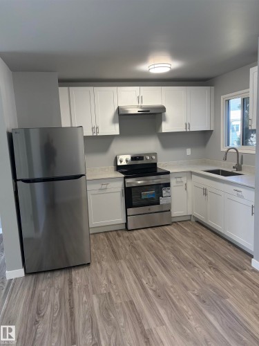 Kitchen featuring wood-finish flooring, white cabinetry, stainless steel appliances, and light-toned countertops - 14075 30 Street E, Edmonton, AB - Indoor Photo Showing Kitchen
