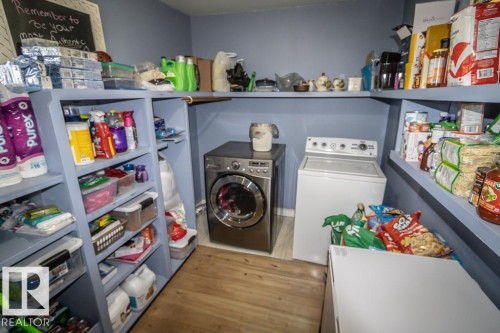 Dedicated laundry space featuring a front-loading washing machine, top-loading washing machine, wood-finish flooring, built-in shelving, and pale blue wall paint - 4814 51 Ave, St. Paul Town, AB - Indoor Photo Showing Laundry Room