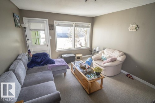 Carpeted living space featuring neutral wall tones, a large window, and a white door with glass paneling - 4814 51 Ave, St. Paul Town, AB - Indoor Photo Showing Living Room