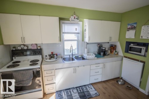 Kitchen featuring wood-finish flooring, white cabinetry, a double basin sink, and a built-in microwave niche - 4814 51 Ave, St. Paul Town, AB - Indoor Photo Showing Kitchen With Double Sink