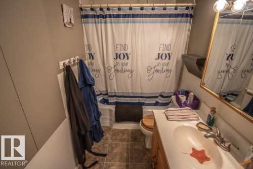 Bathroom featuring a white bathtub and shower combination, a vanity with an integrated sink, a large mirror with a gold-tone frame, and tile flooring - 4814 51 Ave, St. Paul Town, AB - Indoor Photo Showing Bathroom