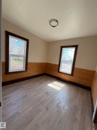 Room featuring half-height wood paneling, and two windows with dark trim. - 