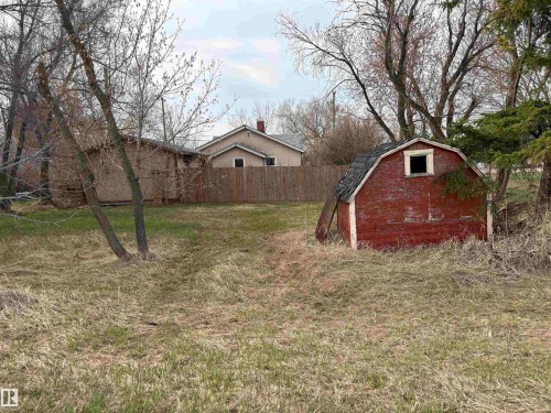 Additional backyard, located behind the fence .Red-painted storage shed with a gambrel roof and a single window opening. - 4622 50 Avenue, Elk Point, AB - Outdoor