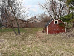 Additional backyard, located behind the fence .Red-painted storage shed with a gambrel roof and a single window opening. - 